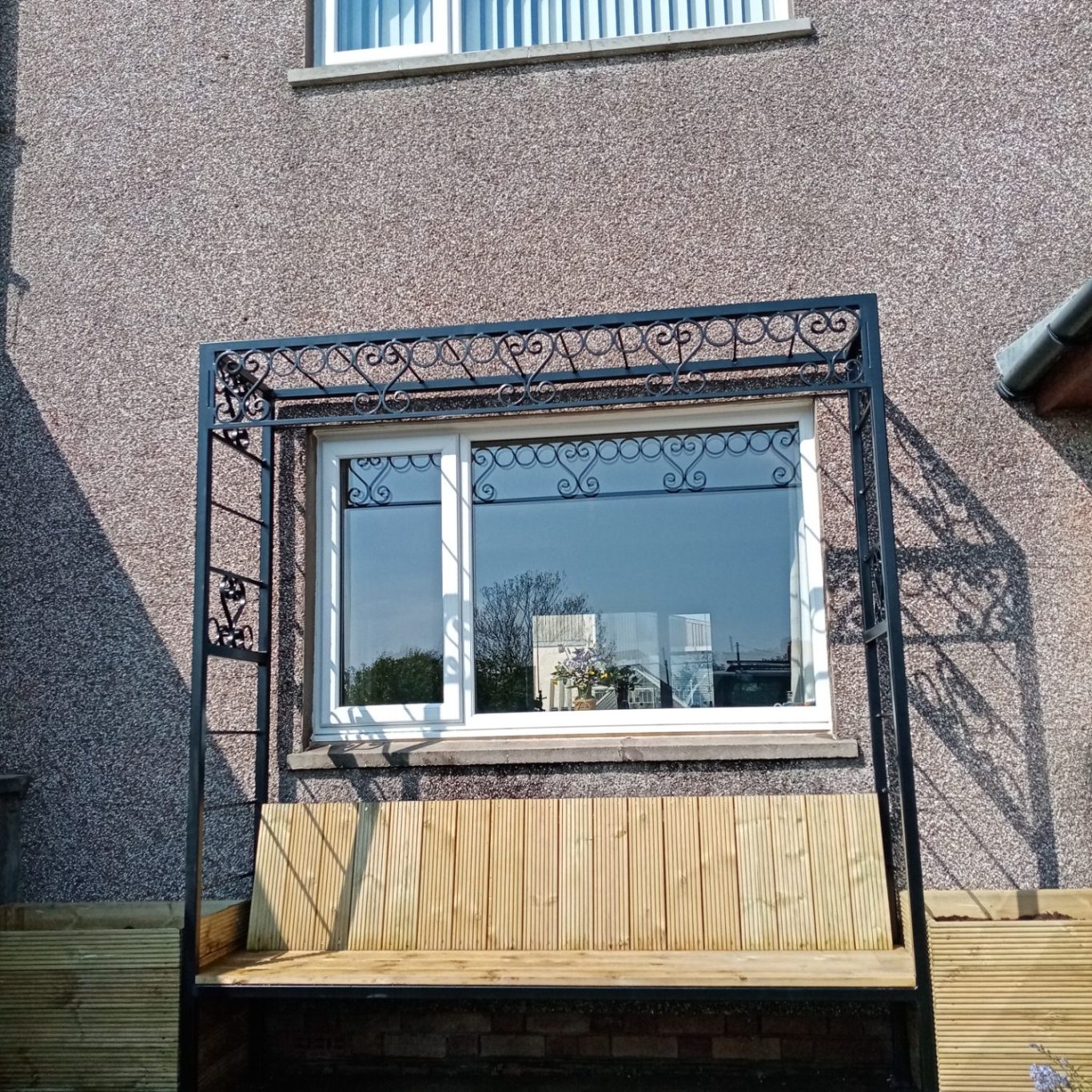 A powder coated black square arbour with rings and scrolls, it has planters either side and a bench incorporated into the middle.