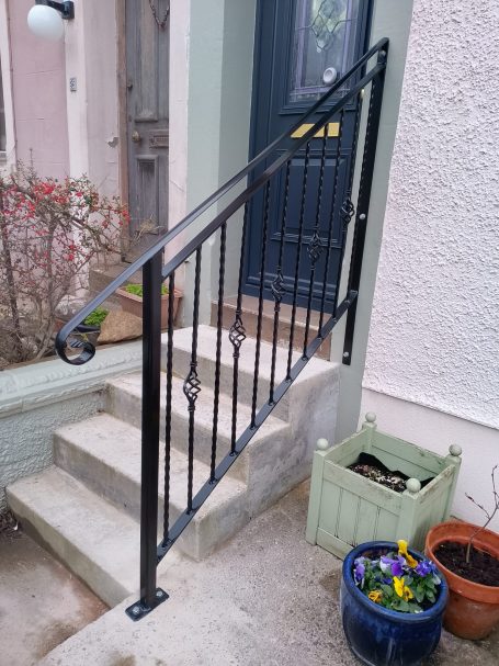 Black metal handrail alongside stairs, with a potted plant nearby.