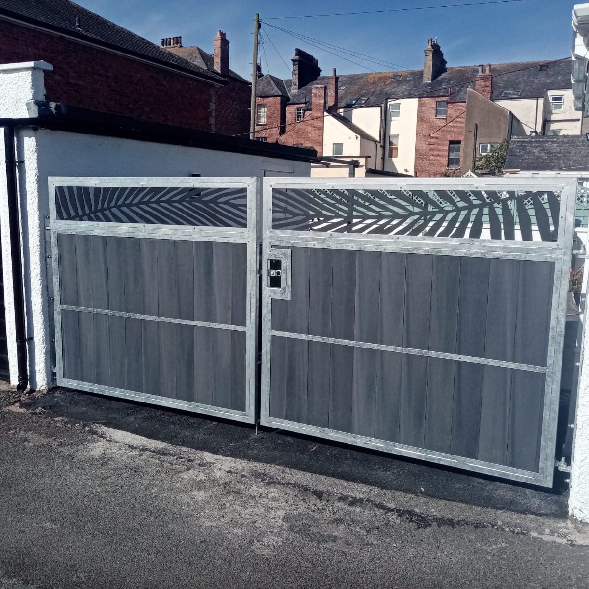 A pair of driveway gates with a leafy pattern in the top, galvanised steel frame with grey composite infills