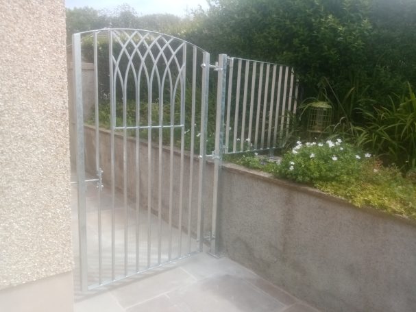 Galvanised metal pedestrian gate against a garden wall