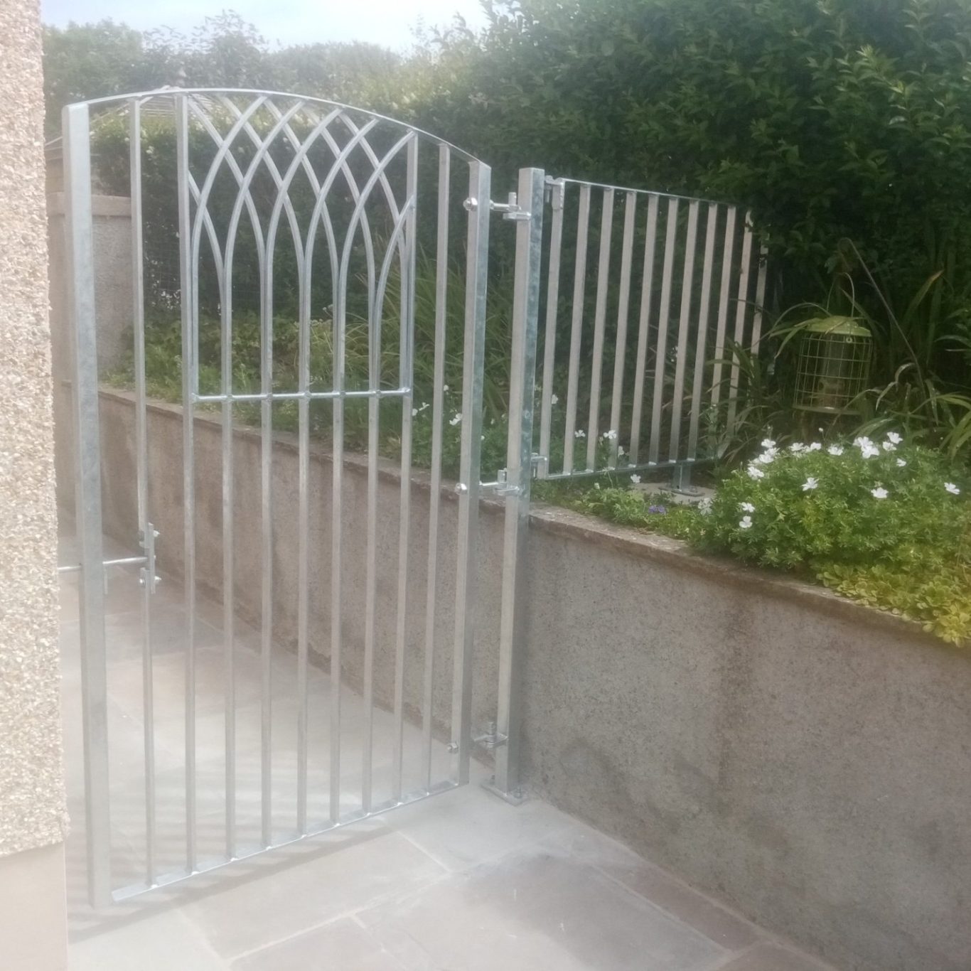 A tall garden gate with a wall top fence panel beside it, all made from galvanised steel with a spring bolt latch